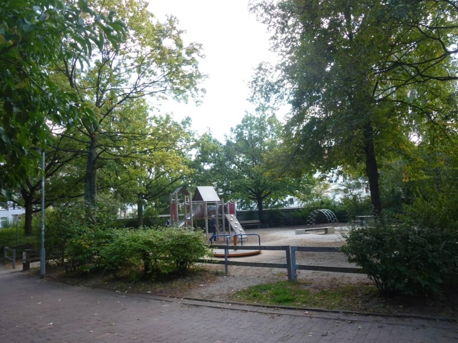 Spielgeräte auf einem von Bäumen und Büschen umgebenen Spielplatz