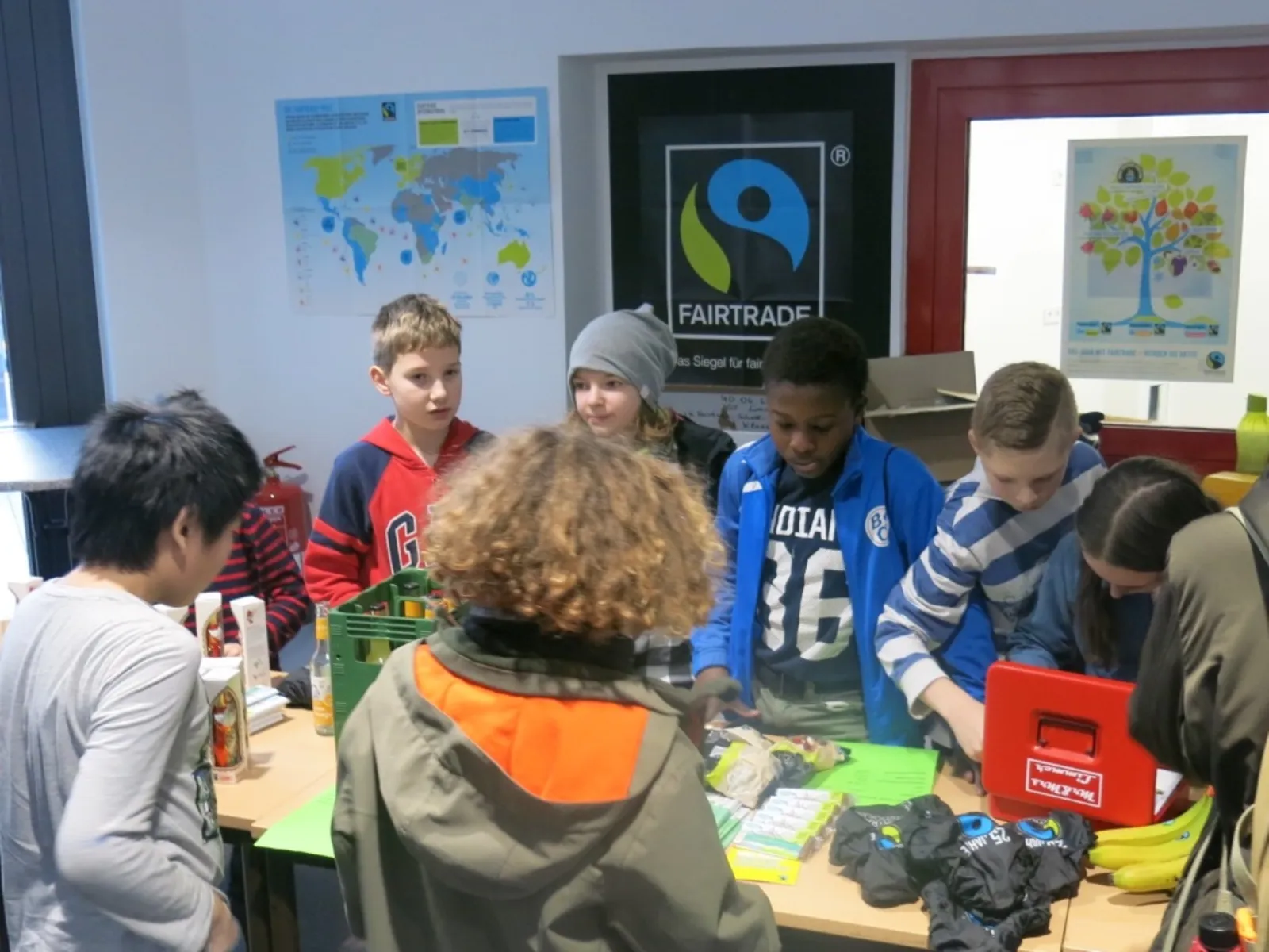 An einer Tischreihe bieten Schülerinnen und Schüler fair gehandelte Produkte an.