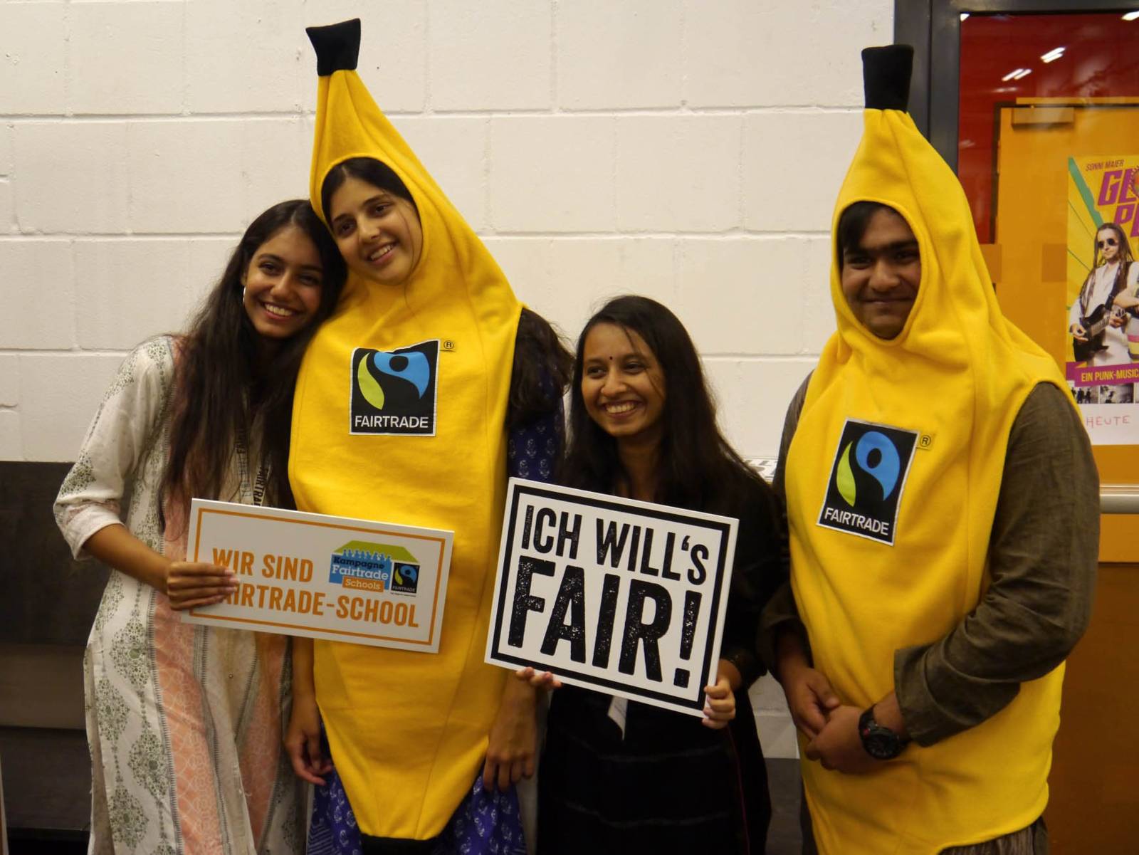 Vier junge Menschen. Zwei halten Schilder, zwei stecken in Bananen-Kostümen. 