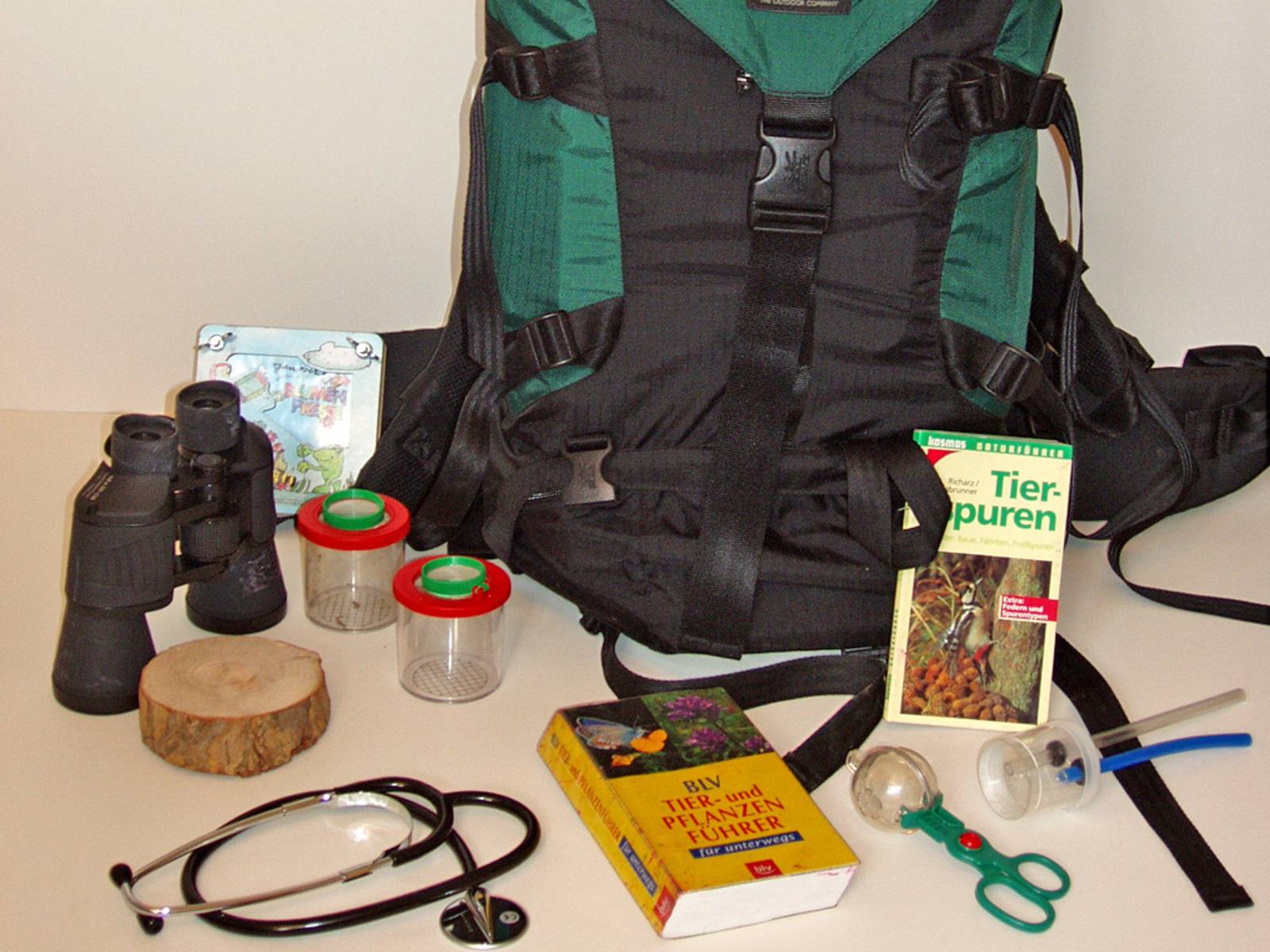 Ein Rucksack mit Büchern, Stethoskop, Fernglas, Probenbehältern und weiteren Erkundungsutensilien