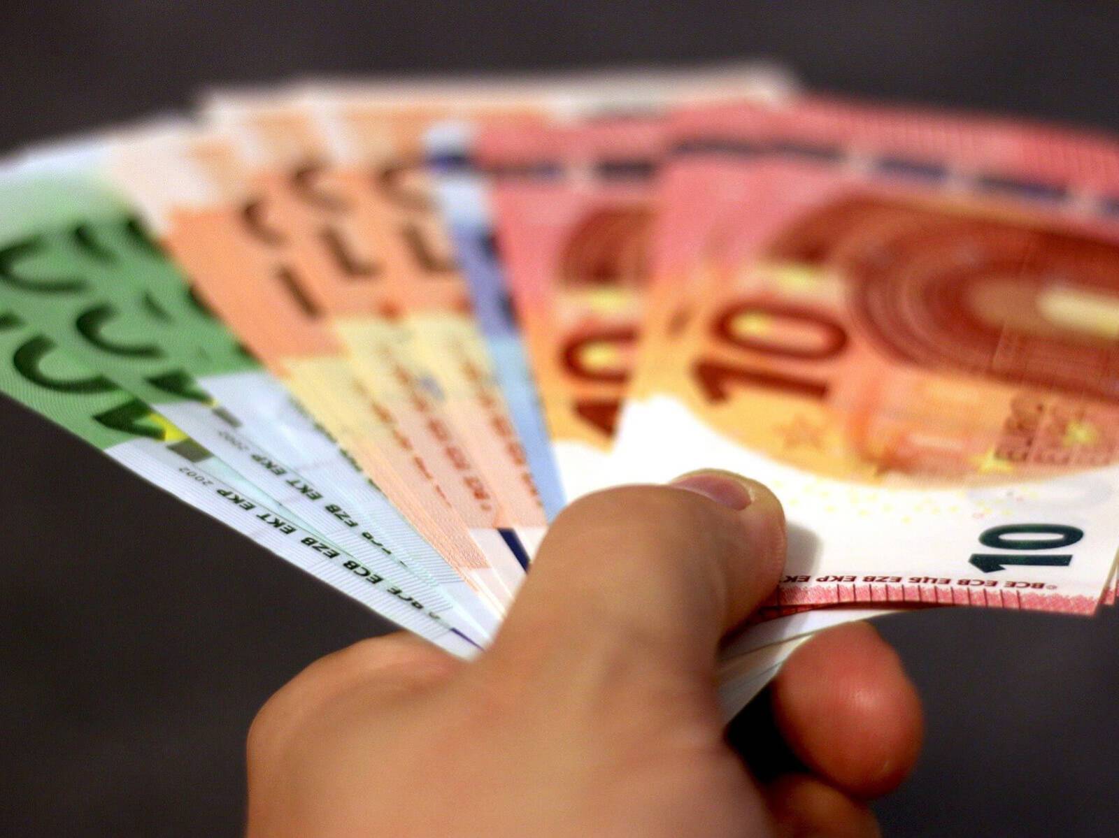 Aufgefächerte Euroscheine in einer Hand vor schwarzem Hintergrund.