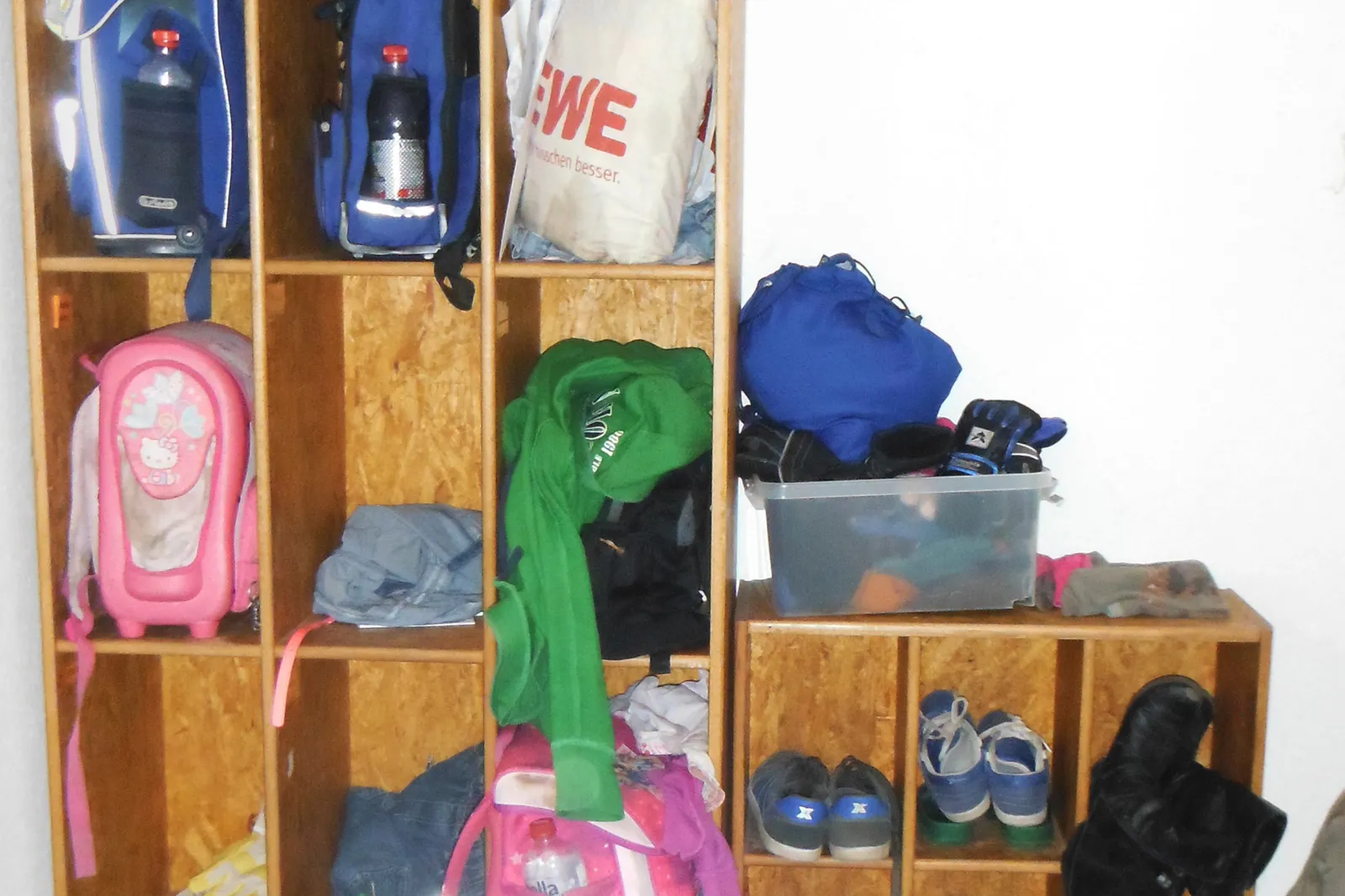 In einem Holzregal sind Rucksäcke und Schuhe von Kindern und Jugendlichen verstaut.