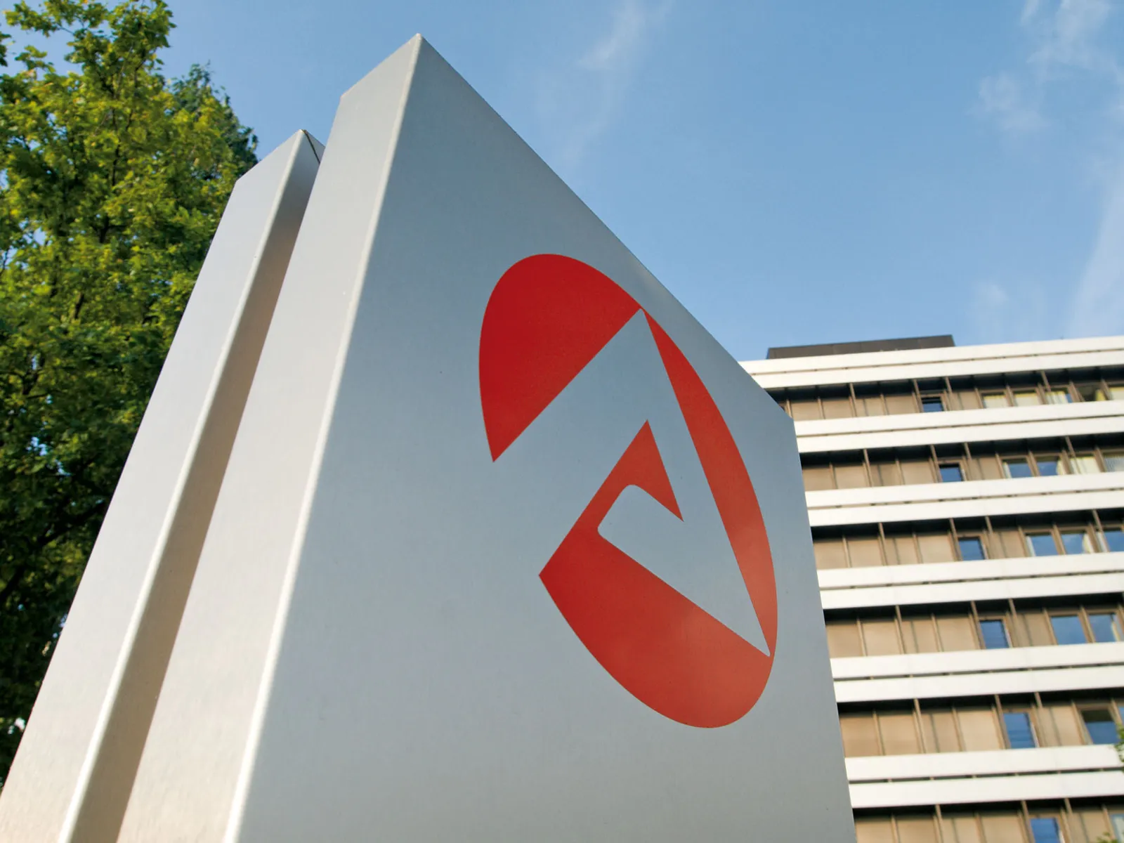 Logo der Bundesagentur für Arbeit auf einer Säule, im Hintergrund ein großes Gebäude.