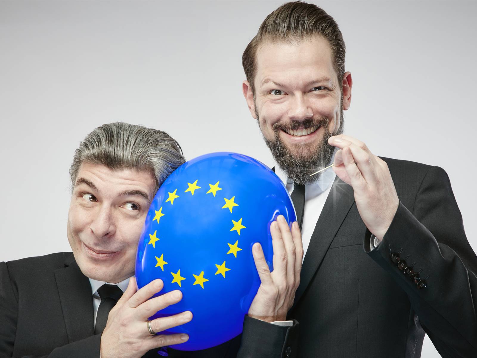 Zwei Männer, einer hält einen Europa-Luftballon, der andere eine Nadel.
