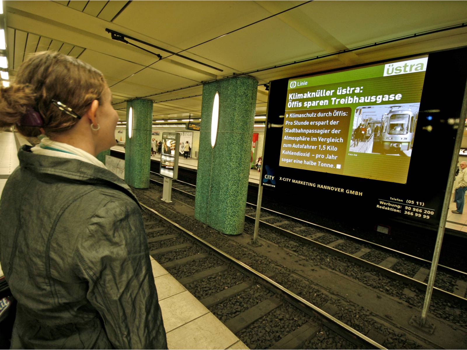 Frau sieht sich eine Nachricht auf einer Leinwand in einer U-Bahnstation an.