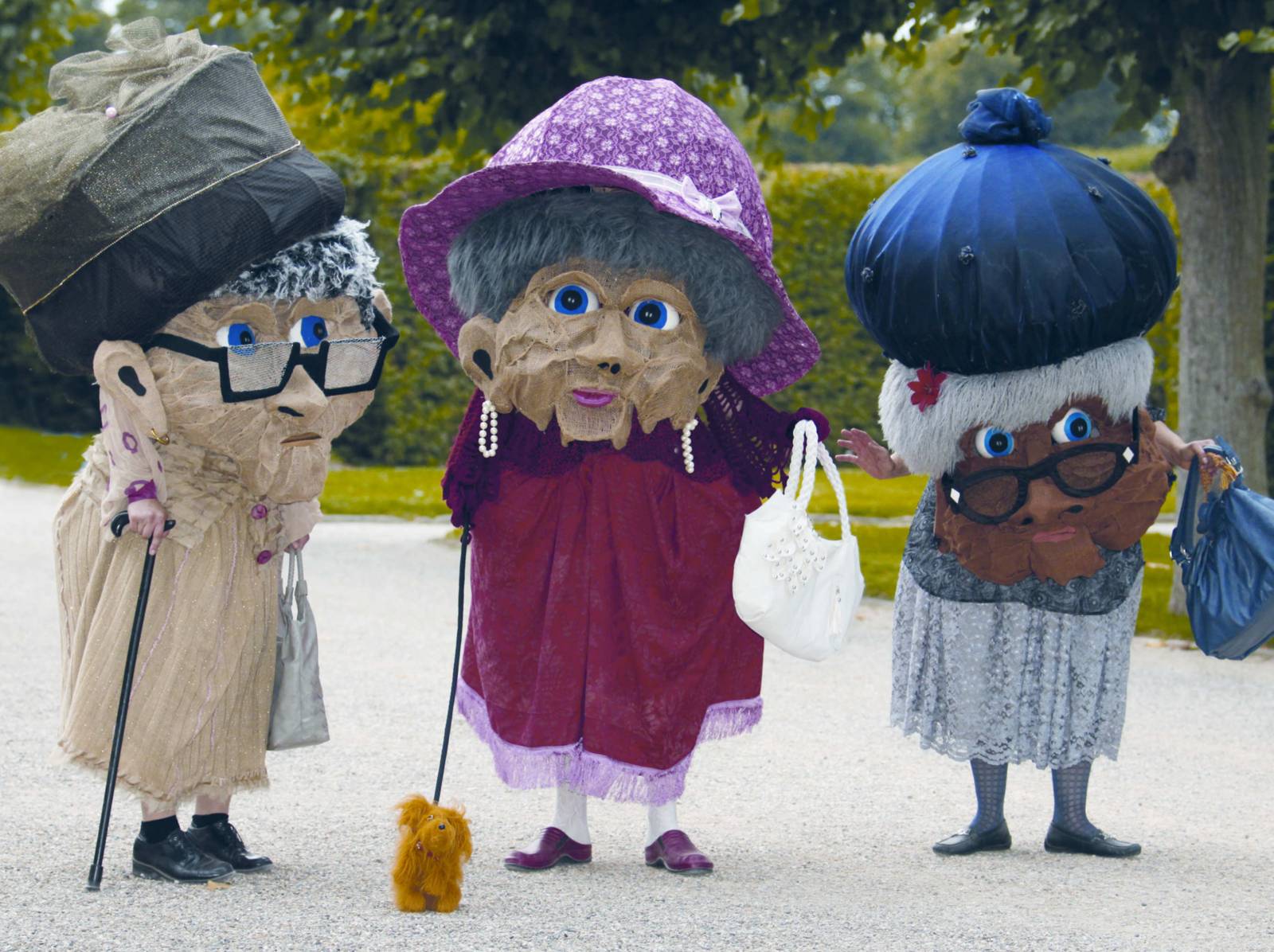 Drei mit riesigen Masken als alte Damen verkleidete Darsteller.