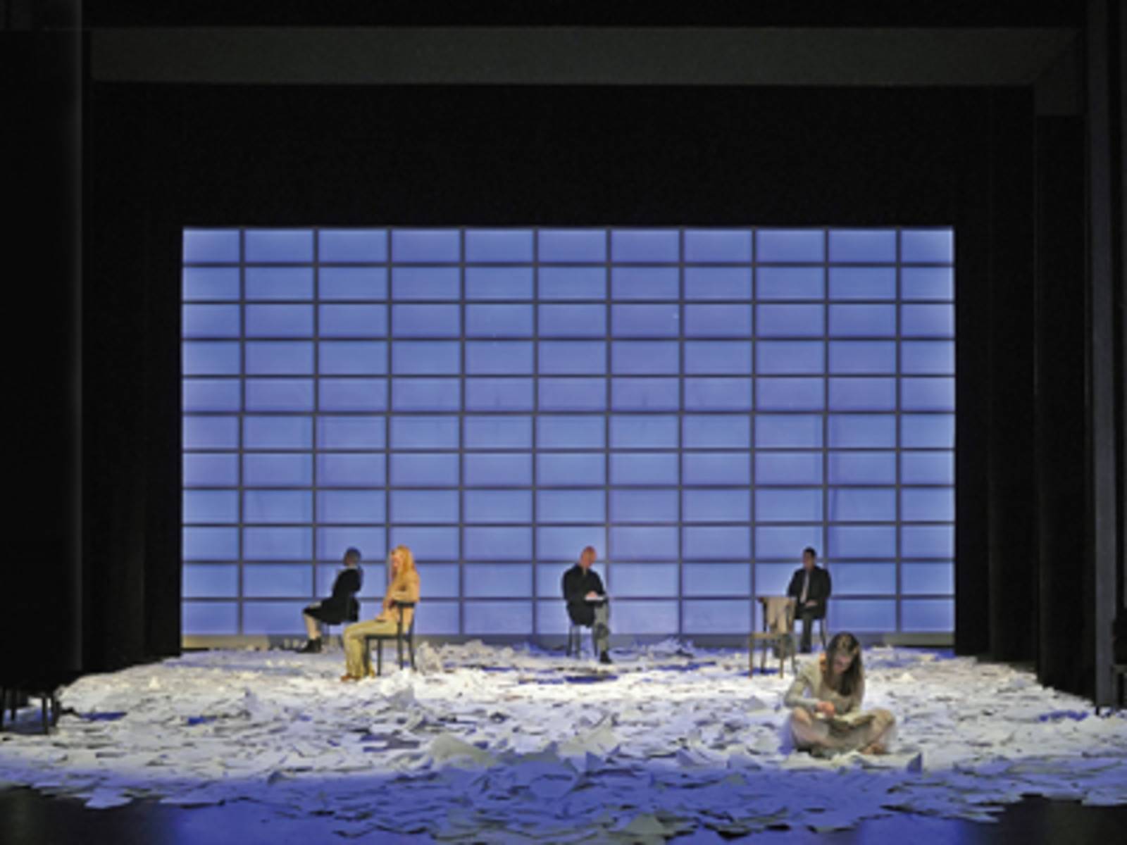 Schauspieler sitzen auf einer Bühne voll von Papierbögen.