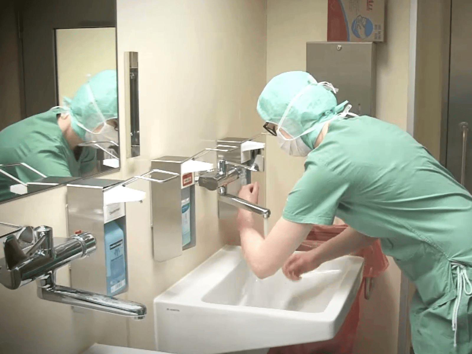 Eine Person in Arztkleidung wäscht sich die Unterarme.