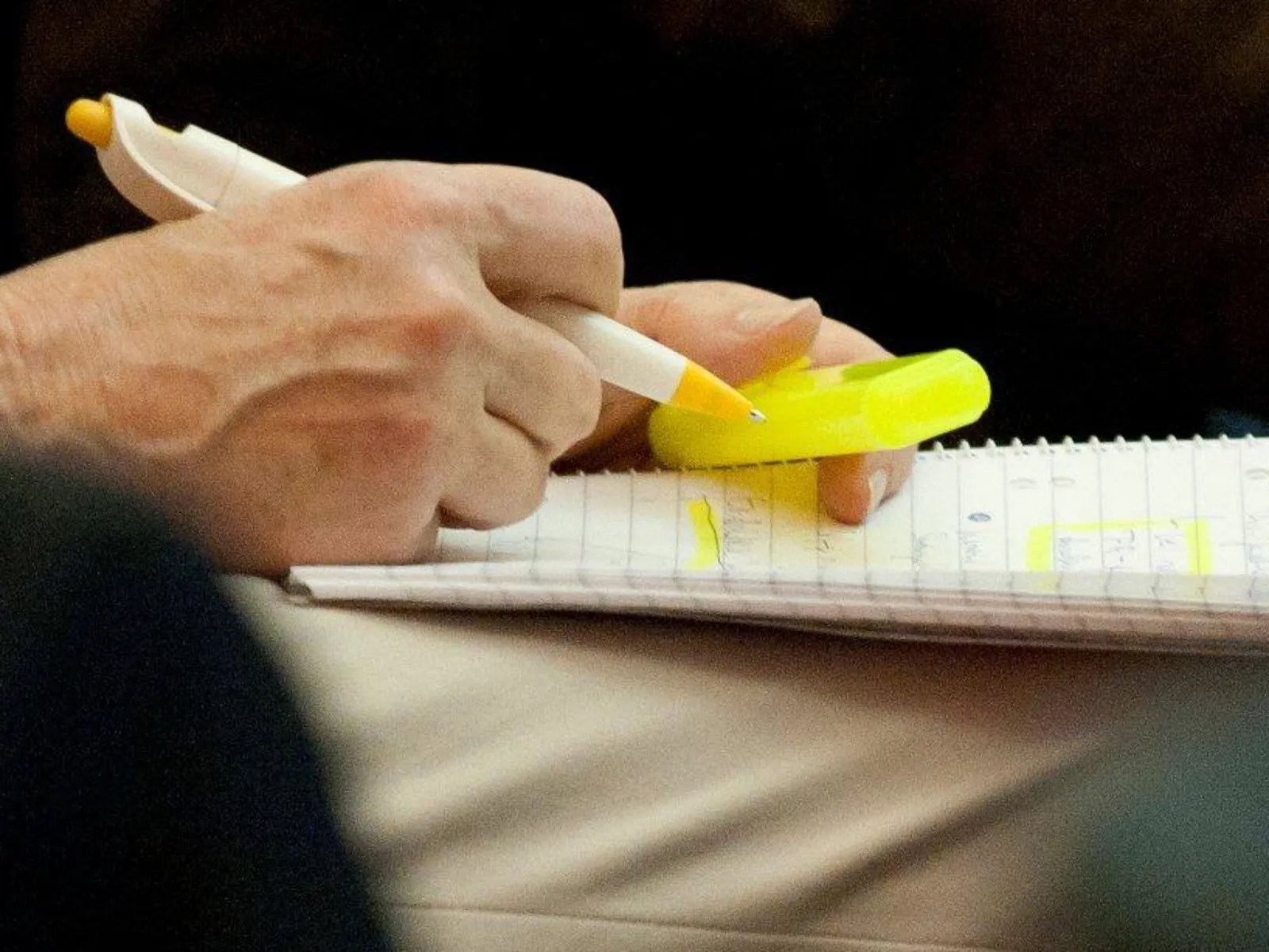 Jemand sitzt auf einem Stuhl, hält einen Schreibblock auf den Beinen und einen Stift in der Hand