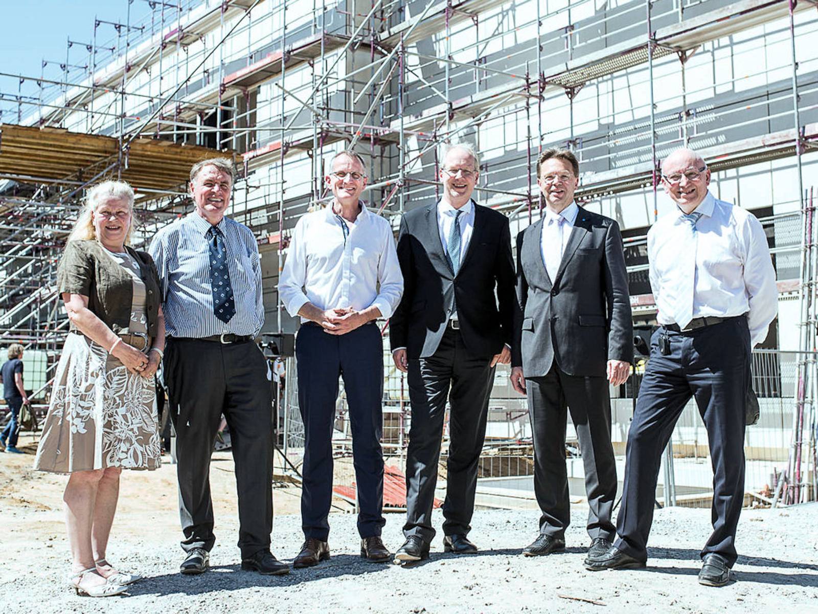 Eine Frau und fünf Männer posieren vor Rohbau eines Gebäudes.