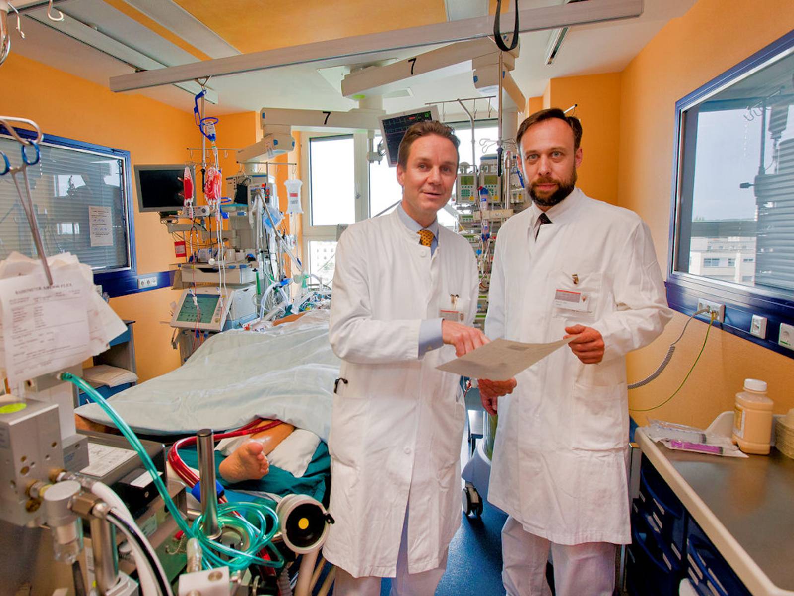 Zwei Männer in weißen Kitteln in einem Raum mit medizinischen Apparaten.