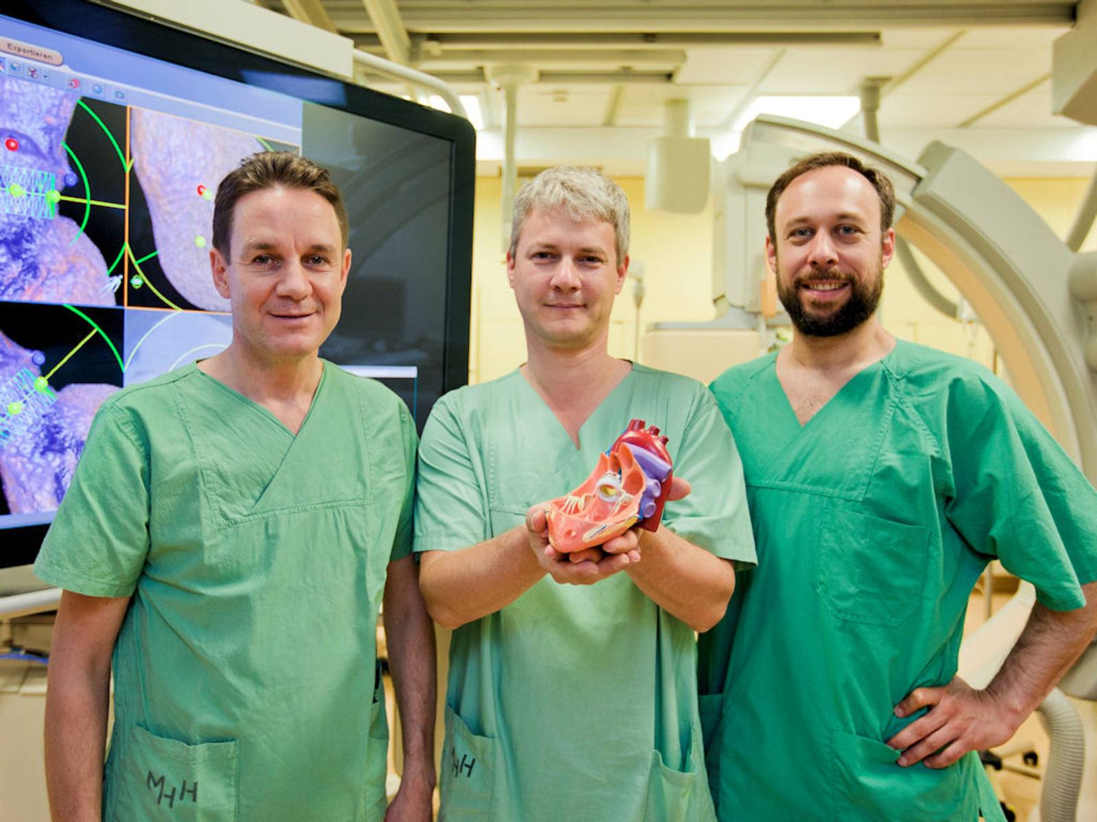 Drei Männer in grünern Kitteln, einer hält ein Modell einer Organs.