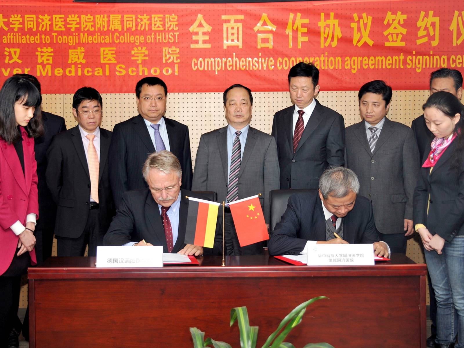 Zwei Männer mit Stiften in den Händen sitzen an einem Schreibtisch, vor ihnen liegen Papiere.