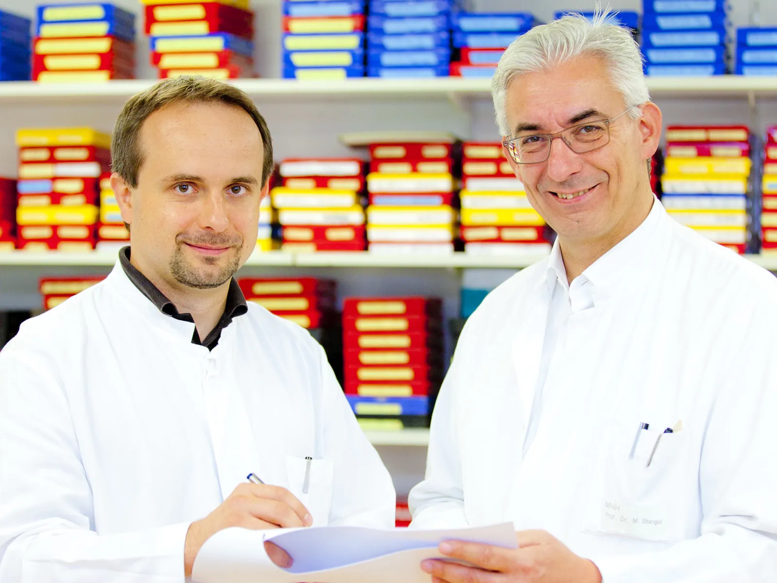 Zwei Männer in weißen Kitteln halten ein Papier und einen Stift in der Hand.