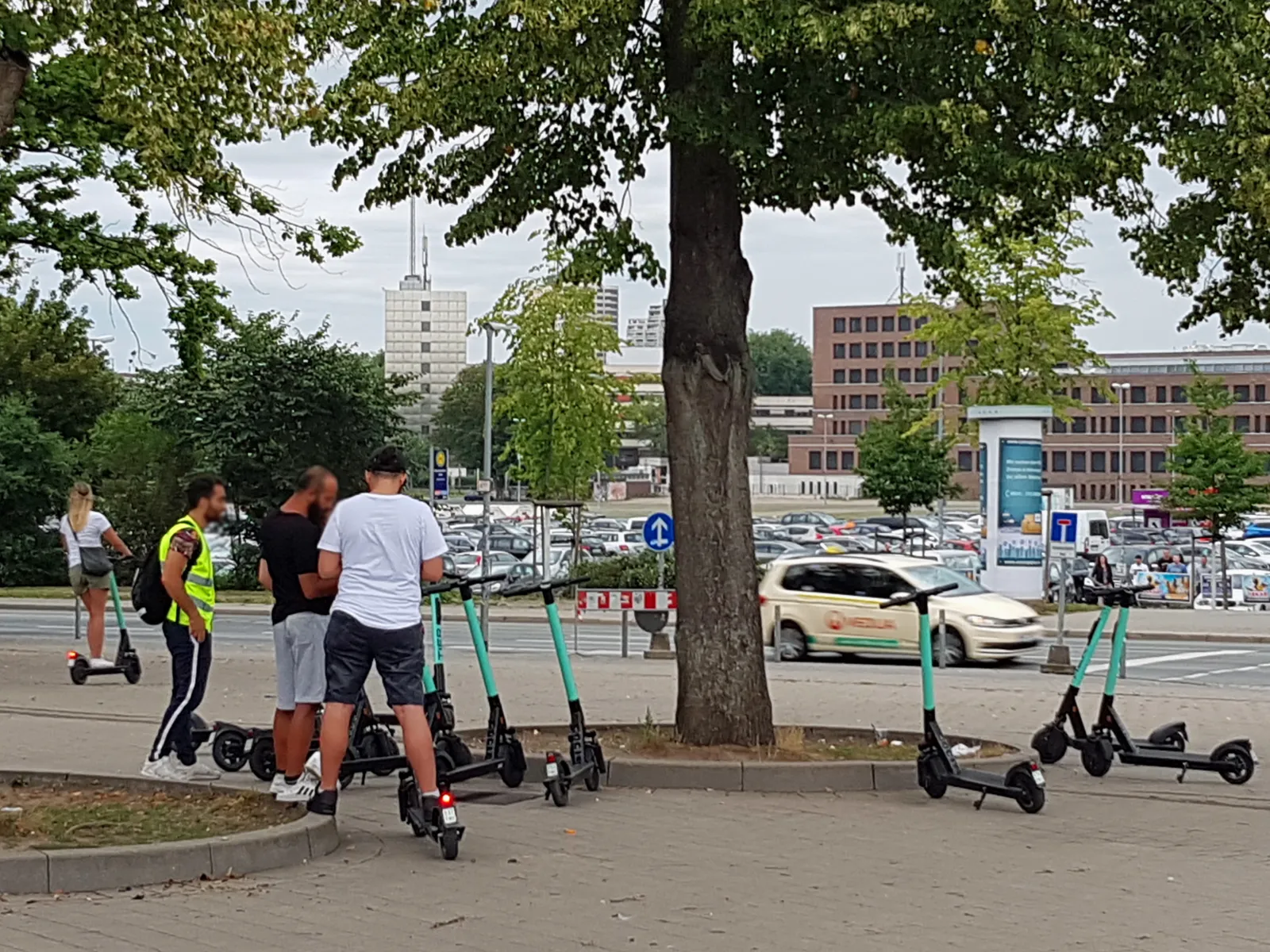 Unter einem Baum stehen Menschen  und Elektroroller