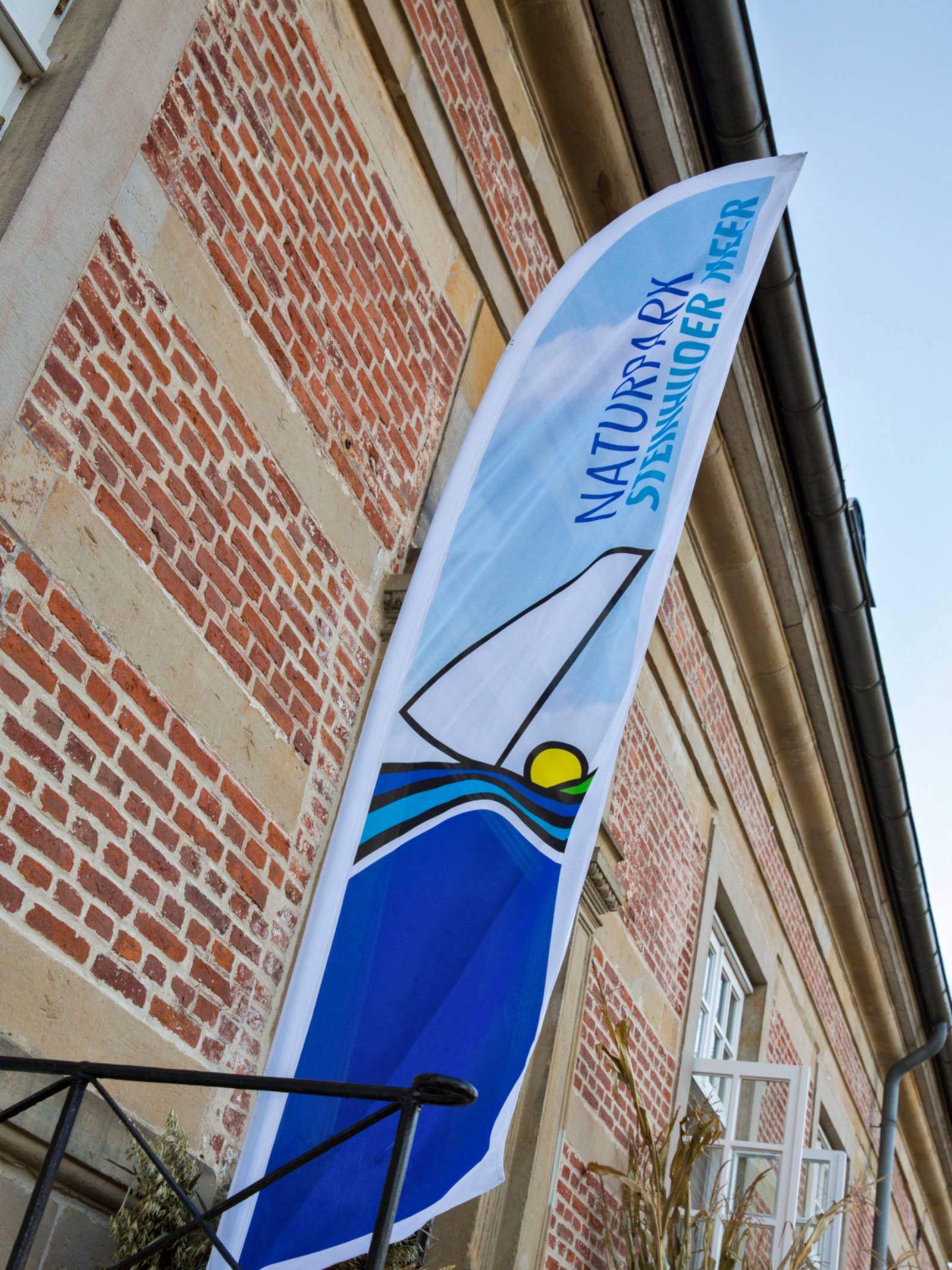 Eine Beachflag mit dem Logo des Naturparks Steinhuder steht vor der Außenmauer von Schloss Landestrost in Neustadt am Rübenberge.
