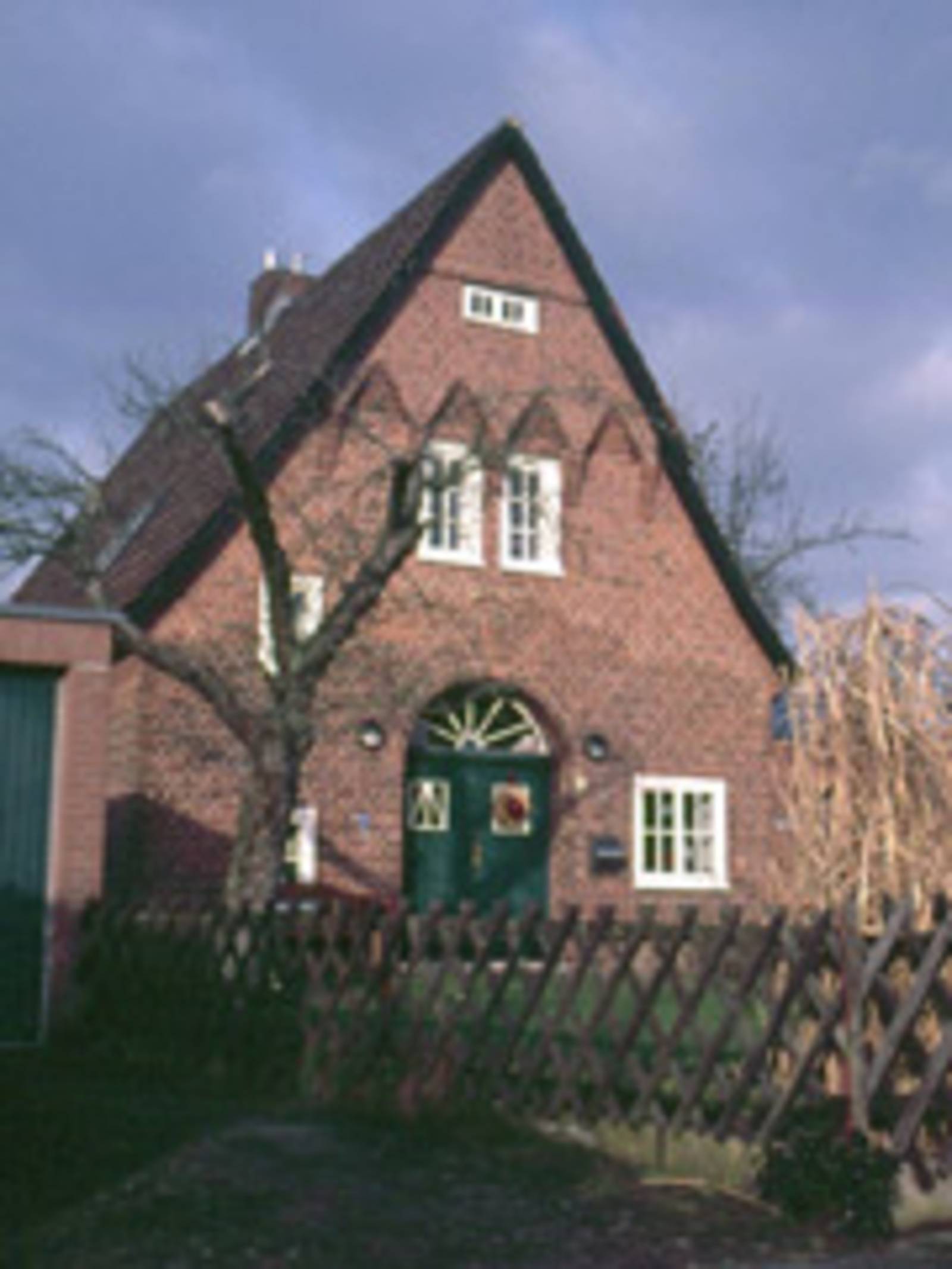 aus rotem Ziegel gemauertes Haus mit grüner Eingangstür und weißen Fensterrahmen
