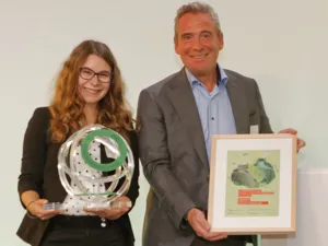 Eine Frau, die eine Troph&auml;e h&auml;lt, und ein Mann, der eine Urkunde h&auml;lt.