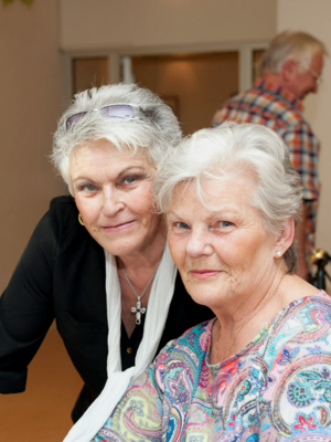 Zwei ältere Frauen halten ihre Köpfe nebeneinander und blicken in die Kamera. 