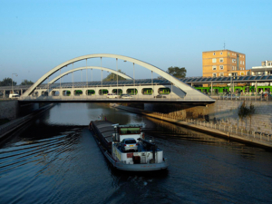 Brücke, auf der Autos und eine grüne Stadtbahn fahren, über den Mittellandkanal, ein Frachtschiff auf dem Kanal, in Richtung Brücke fahrend