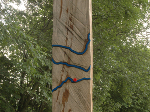 Senkrecht stehender Holzbalken mit blauen Metallwellen, die ein größeres Gewässer symbolisieren
