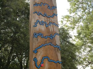 Holzbalken mit blauen Metallwindungen, die einen Flusslauf symbolisieren, und einem roten Ortspunkt