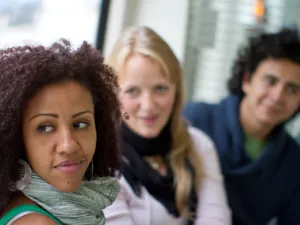 Portraitaufnahme von zwei Frauen und einem Mann. Sie sitzen nebeneinander in der Stadtbahn.