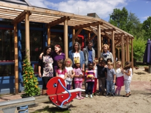 Auf dem Bild sind die Beteiligten des Beschäftigungsprojektes und die Kindergartenkinder auf dem Außengelände der Kita zu sehen. Sie stehen zusammen als Gruppe vor dem Kitagebäude (Erwachsene hinten und die Kinder stehen vor den Erwachsenen).