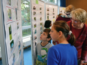 Die Kinder der zwei Klassen der Grundschule Hägewiesen suchen gemeinsam mit ihren "Beraterinnen" aus über 100 Fotos, die für sie besonderen Bilder aus. Die Bilder sind an mehreren Pinwänden befestigt.