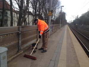Auf dem Bild ist ein Mann zu sehen, der mit einem Besen den Bahnsteig reinigt.