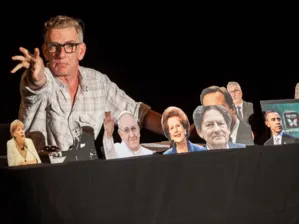 Mann auf B&uuml;hne mit diversen Politiker-Portraits.
