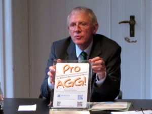 Ein Mann am Ende eines Tisches hält ein DinA4-großes SIegel hoch, auf dem steht "Pro-AGG - Diese Diskothek unterstützt und respektiert das Allgemeine Gleichbehandlungsgesetz".