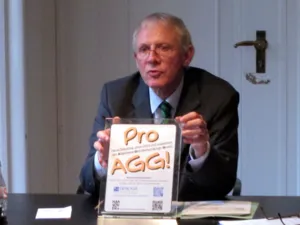 Ein Mann am Ende eines Tisches h&auml;lt ein DinA4-gro&szlig;es SIegel hoch, auf dem steht "Pro-AGG - Diese Diskothek unterst&uuml;tzt und respektiert das Allgemeine Gleichbehandlungsgesetz".