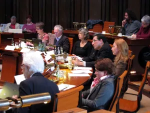 Zw&ouml;lf Personen sitzen in zwei Sitzreihen im Viertelkreis hinter Pulten. Einige schauen in Richtung der SPD-Fraktion auf der gegen&uuml;berliegenden Seite, andere auf vor sich liegende Papiere. Ein Mann schaut in sein aufgeklapptes Notebook.