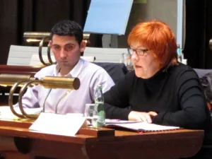 Zwei Personen sitzen hinter Pulten. Die Frau rechts spricht.