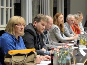 Sieben Personen sitzen nebeneinander und blicken nach vorne.