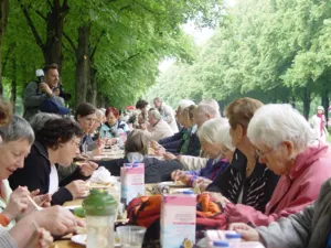 Junge und alte Menschen sitzen gemeinsam zum Essen an einer langen Tafel in der Herrenh&auml;user Allee