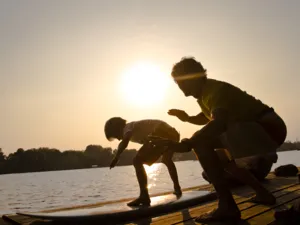 Ein Junge und ein Mann stehen auf einem Surfbrett auf einem Steg.