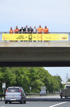 Spannband an Brücke mit Menschen dahinter über vierspuriger Straße