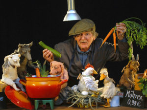 Gerhard Seiler, verkleidet als Gemüsehändler mit Schiebermütze und Schürze, und einige seiner Tierfiguren.