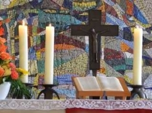 Altar mit Kreuz, Kerzen und einem Pult mit offenem Buch vor einer Mosaikwand