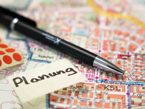 Das Foto ist ein Symbolbild für die Fachplanung. Es ist ein Close-Up mit einer hohen tiefenunschärfe. Das Foto zeigt einen schwarzen Kugelschreiben, der auf einer Stadtkarte liegt. Daneben befindet sich ein "Post-it"-Zettel auf dem Planung geschrieben steht.
