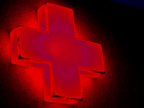 In rot leuchtet ein Kreuz oder Plus-Zeichen an einem Gebäude.
