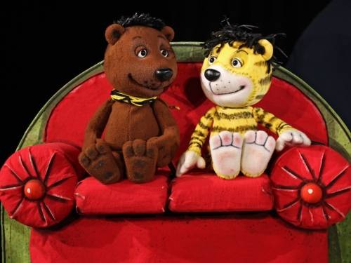 Eine Bären- und eine Tigerpuppe sitzen auf einem großen Sofa.