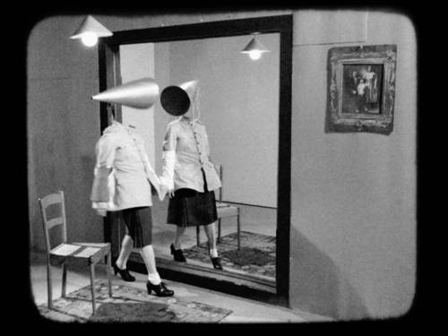 Schwarzweißbild einer Frau, die sich in einem Wandspiegel betrachtet.