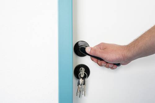 Ausschnitt einer Wohnungstür. Ein Schlüssel steckt im Schloss, eine Hand drückt die Türklinke runter.