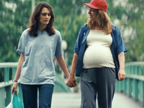 Zwei Frauen gehen Hand in Hand über eine Brücke - eine der beiden ist schwanger