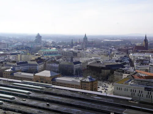 Blick aus der Vogelperspektive auf eine Stadt, vorn Gleise, Bahnsteige und ein breites Gebäude