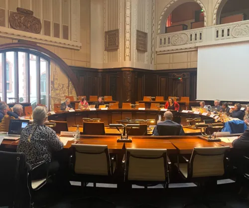 Im finkel vertäfelten aber hell ausgeleuchteten Hodlersaal sitzen Mitglieder des Internationalen Ausschusses an den im Kreis angeordneten Tischen. Zu sehen sind insgesamt 15 Personen.