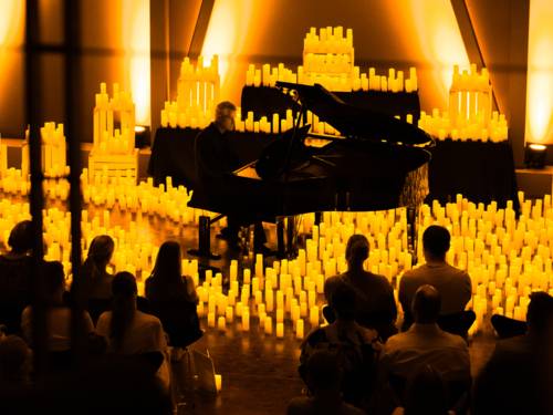 Ein Pianospieler ist von einer Vielzahl von Kerzen umgeben und spielt vor Publikum.